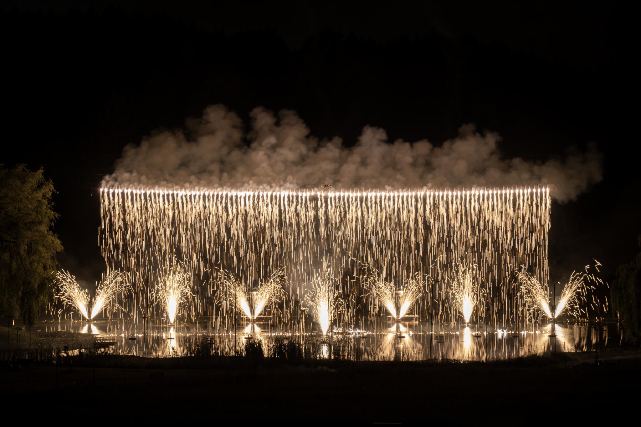 White fireworks pour down (mimicking a waterfall) and small yellow streams burst forth from the ground. This all takes place over water.